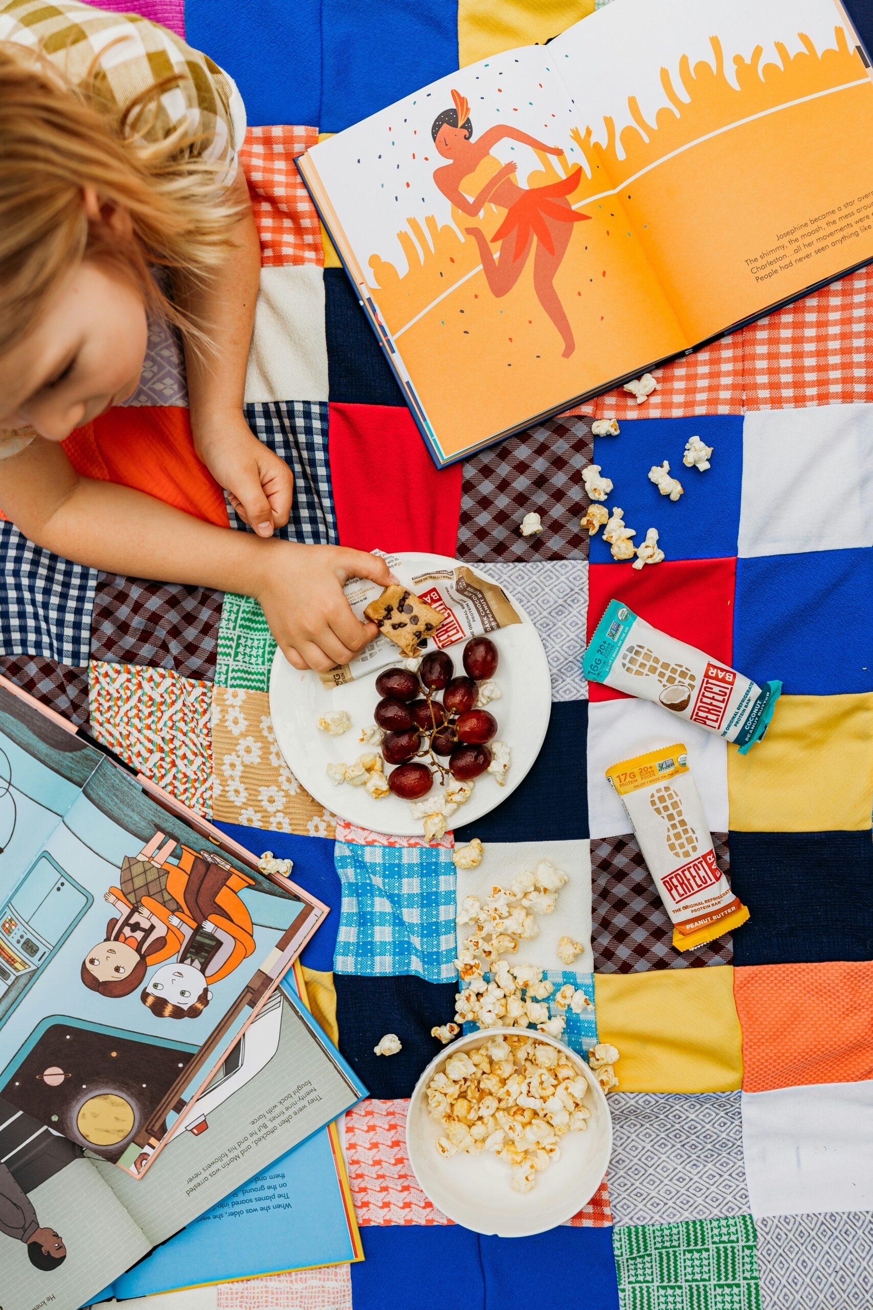 A young child eating a simple snack plate outdoors, holding a white ceramic plate with fruit and crackers.